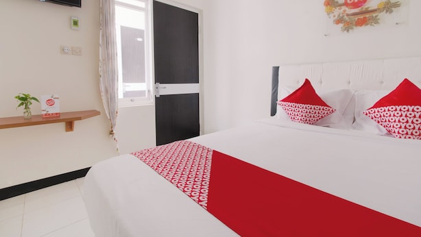 A hotel room with a bed, a television mounted on the wall, a door, and a shelf with a plant and a sign. - Hotel O Cozy Residence Syariah (Malang)