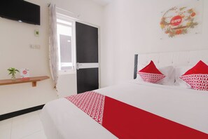 Habitación de hotel con cama, televisión montada en la pared, puerta y estante con una planta y un cartel.