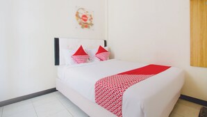 A neatly made bed with white and red bedding, a wooden headboard, and a small decorative item on the wall. - Hotel O Cozy Residence Syariah (Malang)