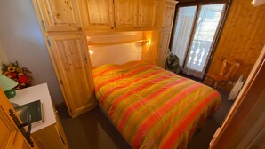 A small, cozy room with a bed, wooden cabinets, a desk, and a window with curtains. - Charming duplex with balcony, near ski and shuttle, parking, WIFI (Châtel)