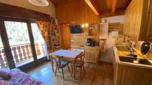 A cozy cabin-style room with a wooden interior, a dining area with a table and chairs, a kitchenette with a stove and sink, and a television mounted on the wall. - Charming duplex with balcony, near ski and shuttle, parking, WIFI (Châtel)