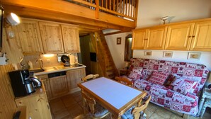 A cozy kitchen with wooden cabinets, a dining table, and a patterned sofa. - Charming duplex with balcony, near ski and shuttle, parking, WIFI (Châtel)