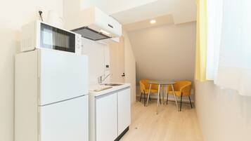 Una cocina compacta con microondas, lavamanos y un pequeño comedor con una silla amarilla.