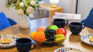 A dining table with a fruit bowl, plates, and blue mugs.