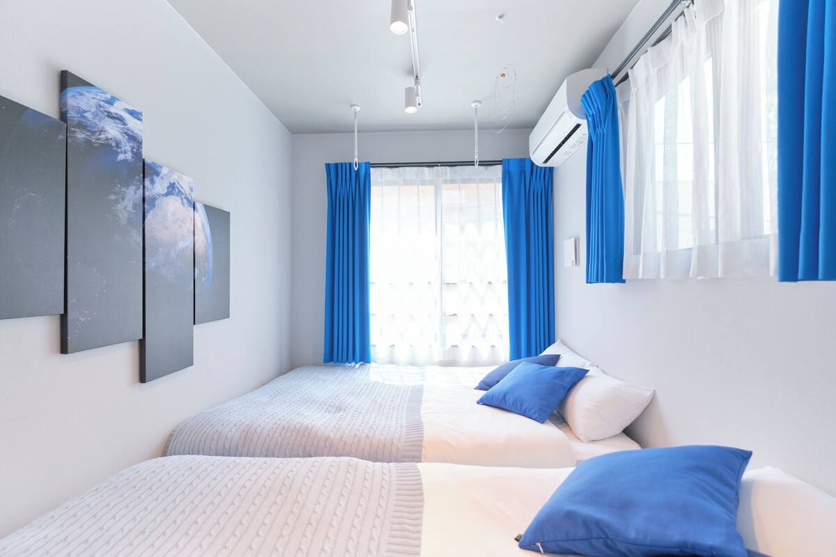 Una habitación de hotel moderna con dos camas, un ventanal con cortinas azules y un aire acondicionado instalado en la pared.