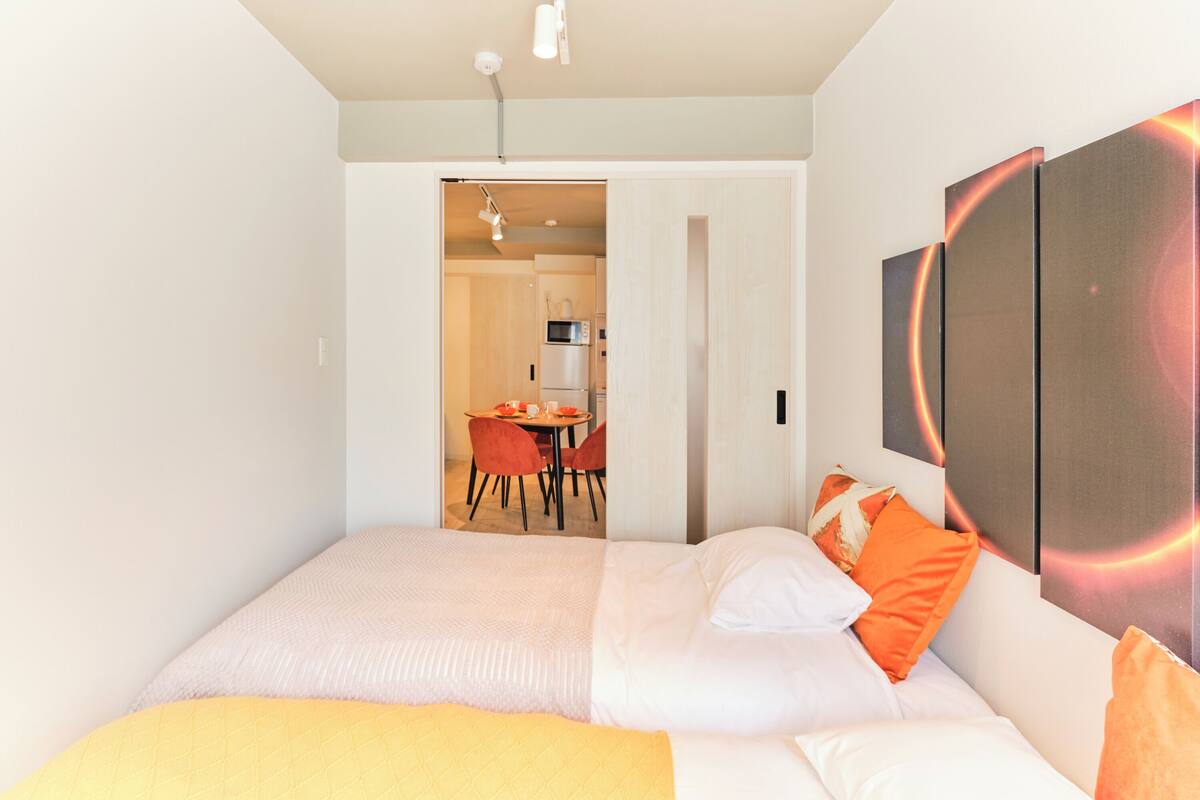 Una habitación de hotel moderna con una cama grande, un área de comedor visible a través de una puerta abierta y un televisor montado en la pared.