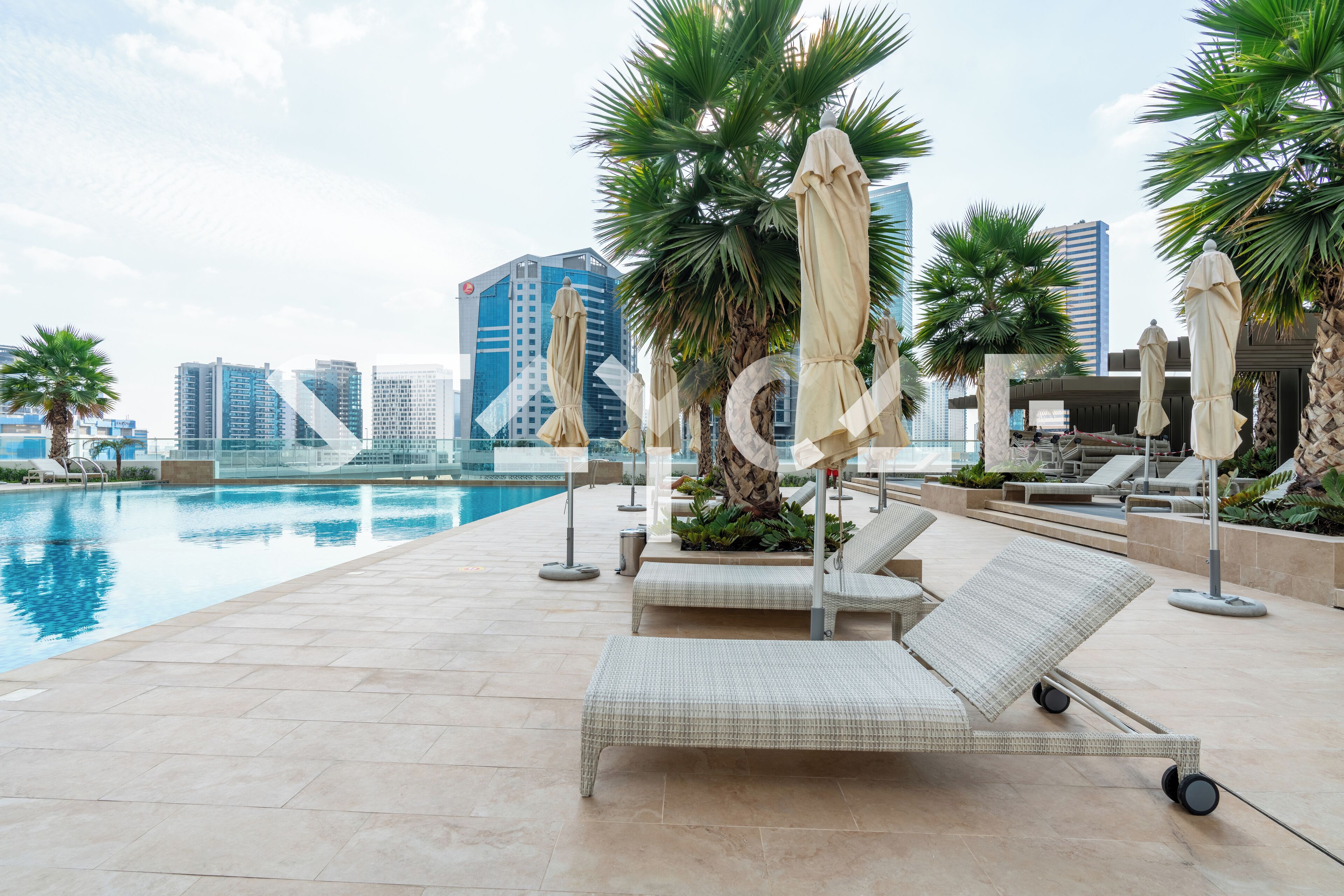 Un espace piscine aménagé sur le toit, avec des chaises longues et des parasols, offrant une vue panoramique sur la ville et ses gratte-ciel.