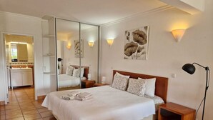 Ein Hotelzimmer mit einem großen Bett, einem Nachttisch, einer Nachttischlampe, einem Spiegel und Blick ins Bad.
