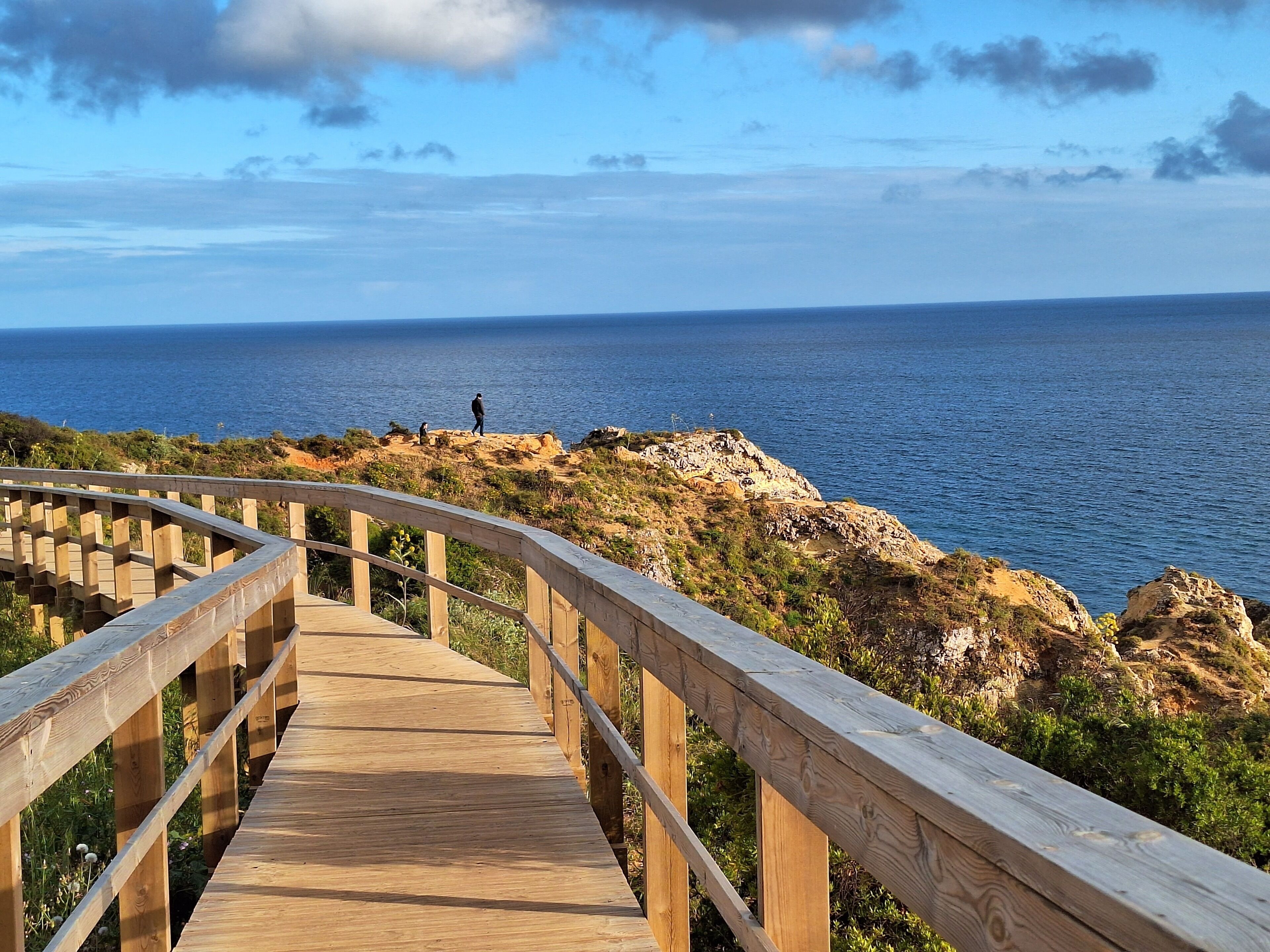 Un paseo marítimo de madera que conduce a una costa rocosa con vistas al mar.