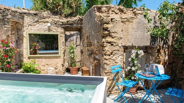 A stone-walled outdoor area with a hot tub, blue folding chairs, and potted plants. - Albergo Rurale Casa Fois (Valledoria)