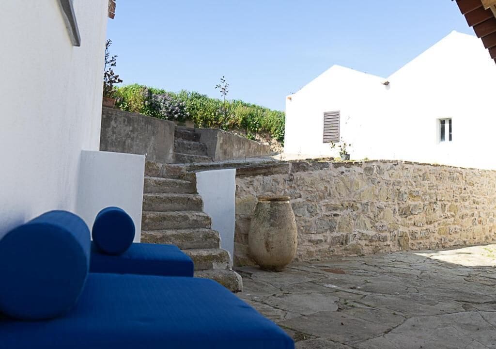 A stone-paved courtyard with a white building, a stone wall, and a large pot.