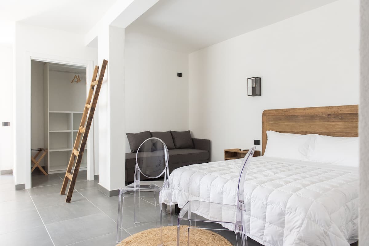 A bedroom with a bed, a wooden headboard, a grey sofa, a wooden ladder, and a wardrobe.