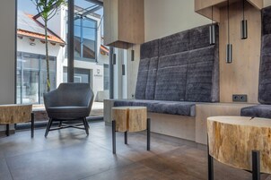 Un interior moderno con un sofá gris, mesas de madera y un ventanal con vistas a un edificio con un letrero que dice "HAMBURGER".