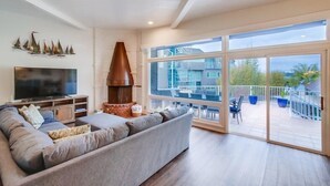 En stue med stor sofa, fladskærms-tv, murstenspejs og balkon med udendørs møbler.