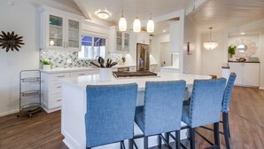 Et moderne køkken med hvide skabe, en central ø med barstole, hængende lamper og et backsplash med mosaikfliser.