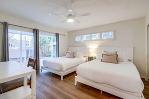 A hotel room with two single beds, a dining table, and a ceiling fan.