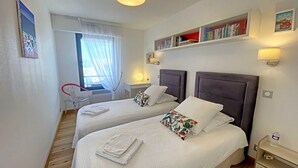 A hotel room with two beds, a desk, a chair, a bookshelf, and a window with curtains. - Penthouse in Lorient Center, 2 Bedrooms with Secure Parking (Lorient)