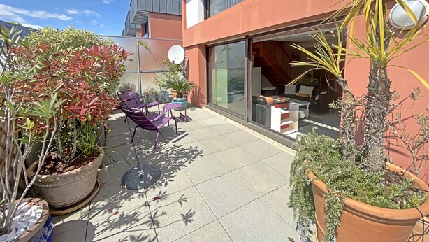 A modern building with a glass door entrance, a patio area with outdoor furniture, and various potted plants. - Penthouse in Lorient Center, 2 Bedrooms with Secure Parking (Lorient)