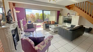 A spacious living room with a fireplace, a large TV, and a staircase. - Penthouse in Lorient Center, 2 Bedrooms with Secure Parking (Lorient)