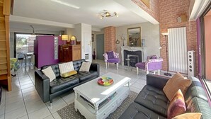 A spacious living room with a fireplace, a black leather sofa, and a coffee table. - Penthouse in Lorient Center, 2 Bedrooms with Secure Parking (Lorient)