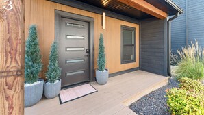 Una casa moderna amb una porta de fusta, dues palmeres en testos i una finestra petita.