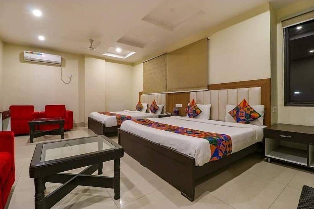 A hotel room with two beds, a glass coffee table, red chairs, and a TV.