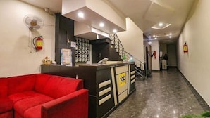 A reception area with a red sofa, a reception desk, a staircase, and a fire extinguisher on the wall. - Hotel AGK (Haridwar)