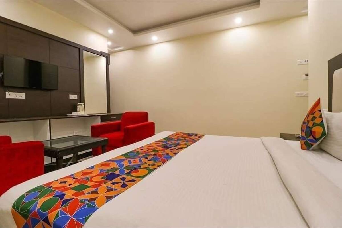 A hotel room with a bed, a TV mounted on the wall, red chairs, and a table.