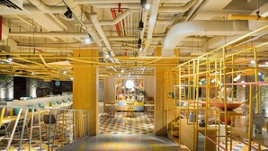 A modern interior with a checkered floor, yellow and white furniture, and exposed pipes on the ceiling. - IKOSHAROLD Suites Seminyak (Seminyak)