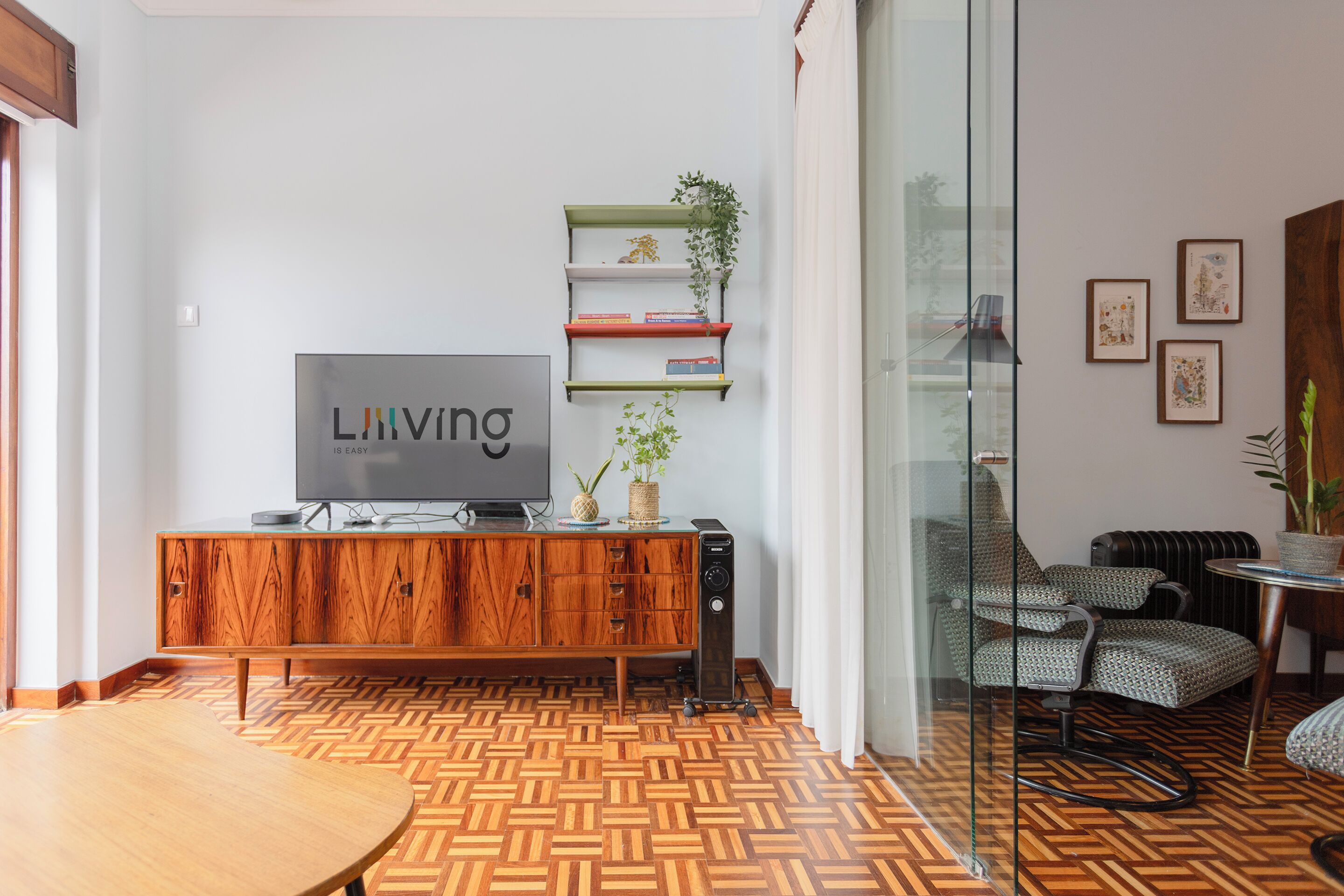 Sala de estar moderna com piso em parquet de madeira, uma televisão sobre um móvel de madeira e uma divisória de vidro.