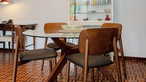 Un comedor con una mesa redonda, sillas de madera, una lámpara colgante y un aparador de vidrio con objetos de colores.