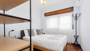 Habitación de hotel ordenada con una cama, un escritorio de madera, una lámpara y un perchero.