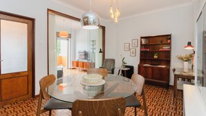 Un comedor con una mesa de vidrio, sillas de madera, una lámpara colgante y una estantería.