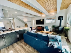 A modern living space with a kitchen, a blue sofa, a TV, and a wood-burning stove.