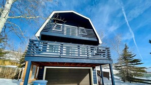 A modern, multi-level house with a garage, a balcony, and a wooden deck.