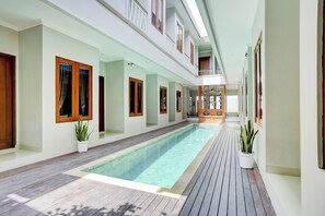 A long indoor swimming pool with wooden flooring, white walls, and multiple windows with wooden frames. - Super OYO Capital O 90291 Vin Stay Petanu (Denpasar)