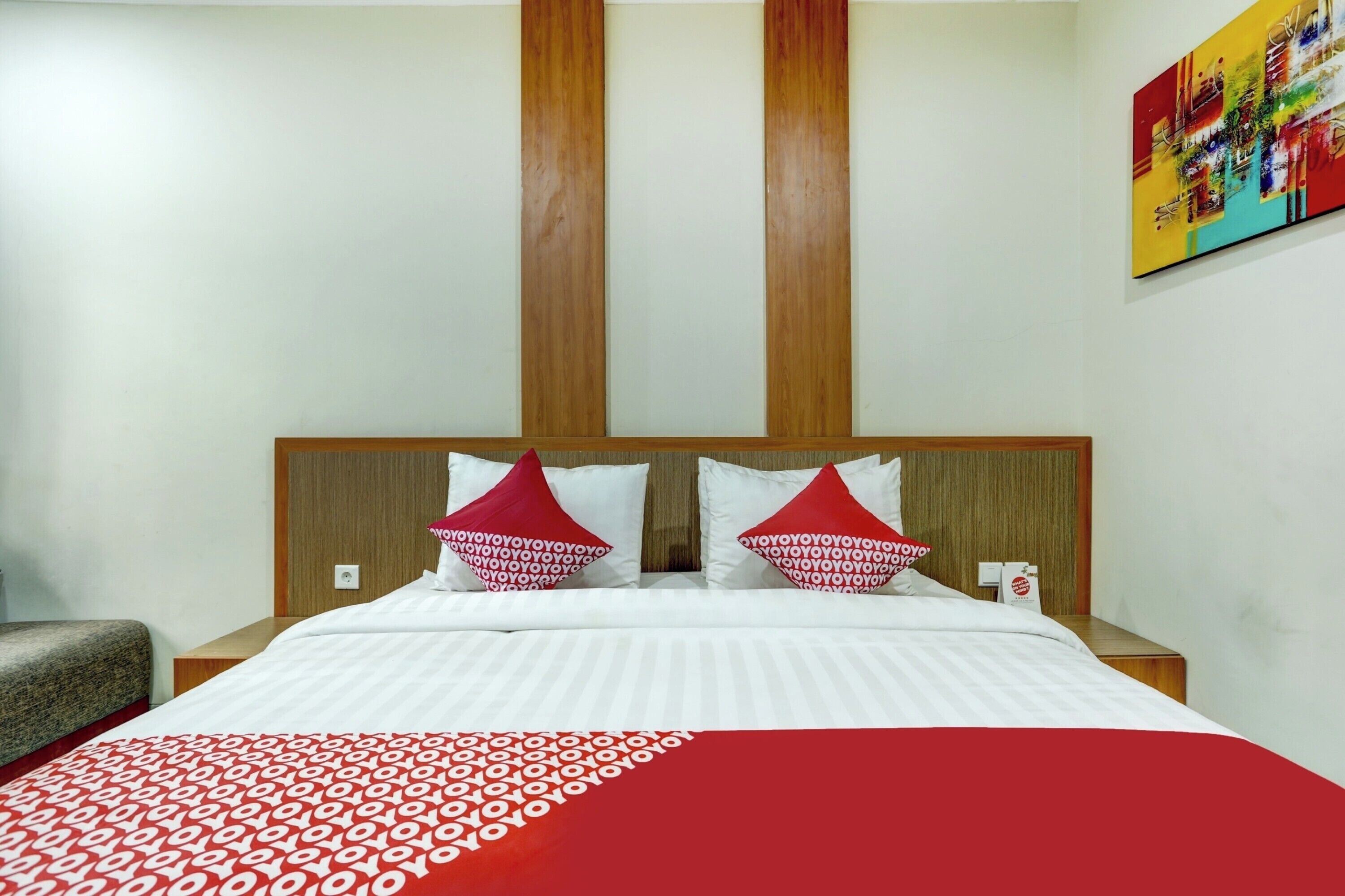 A hotel room with a bed, two pillows, a nightstand, and a painting on the wall.
