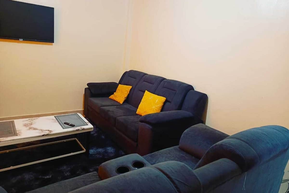 Ein Wohnzimmer mit einem dunkelblauen Sofagarnitur, einem kleinen Couchtisch und einem flachbildfernseher an der Wand.