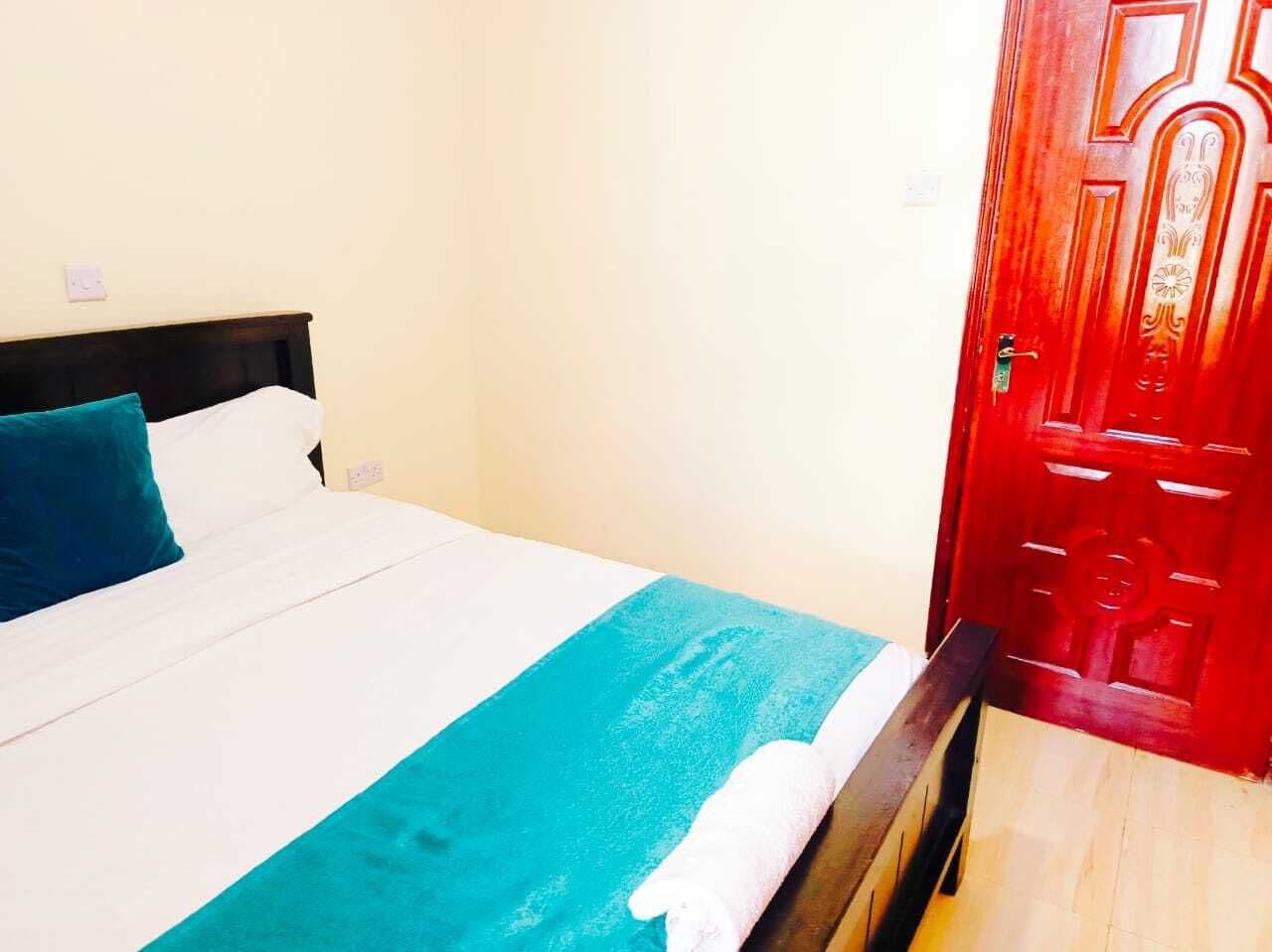 A bed with a white and teal bedspread, a teal pillow, and a white towel on a wooden headboard.