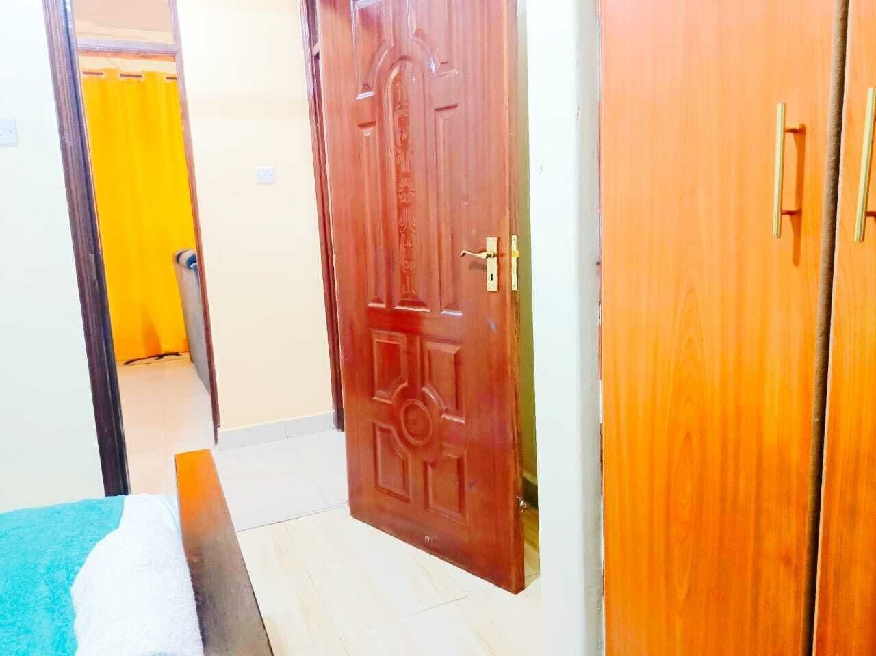 A room with a wooden door, a bed with a blue blanket, and a yellow curtain in the background.