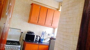 A compact kitchen with wooden cabinets, a gas stove, a microwave, and a small refrigerator. - CH Apartments Kisii (Kisii)