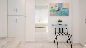 A modern, minimalist room with a white wardrobe, a small black metal chair, a glass shelf with a plant, and a painting on the wall. - Cute and Convenient Studio in Athens (Athens)