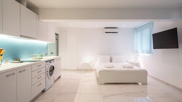 A modern bedroom with a large bed, a washing machine, and a TV mounted on the wall. - Cute and Convenient Studio in Athens (Athens)