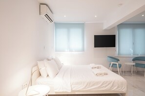 Moderni hotellihuone, jossa on sänky, työpöytä, kaksi tuolia, taulutelevisio ja ikkuna, jossa on sälekaihtimet.