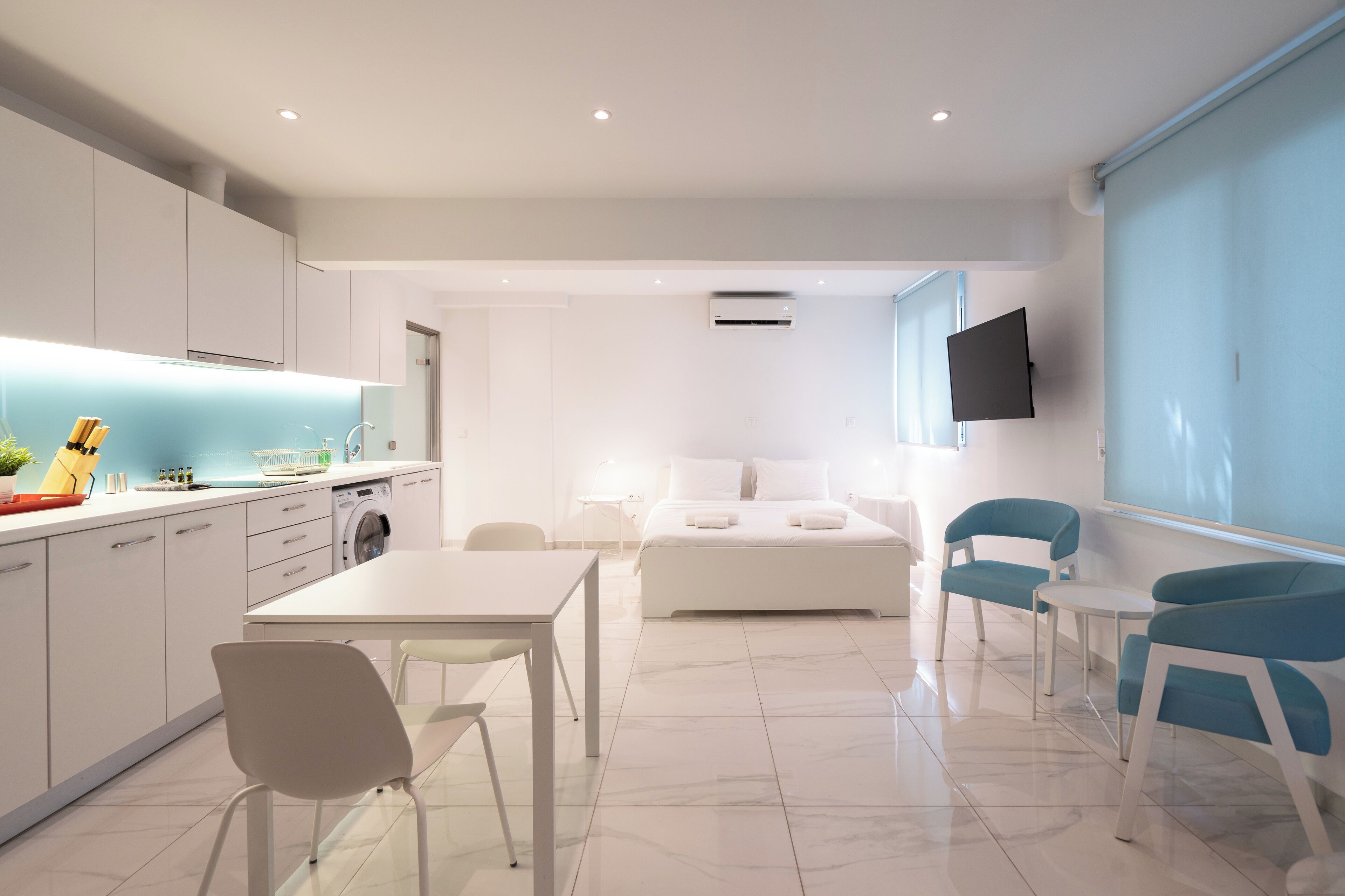 A modern hotel room with a kitchen area, a dining table, and a bed.