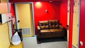 A room with a brown leather sofa, a wooden cabinet, and a red wall.