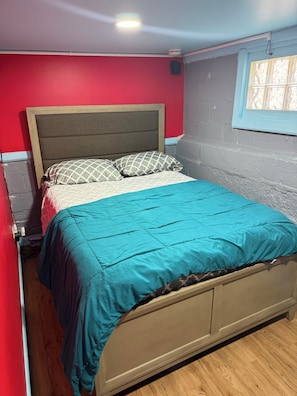 A bed with a teal bedspread and patterned pillows, a wooden headboard, and a window with patterned glass. - Single Room and Bathroom with its own private entrance  (Irvington)