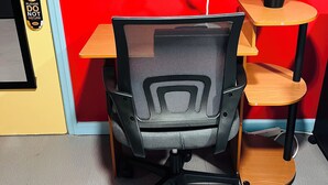 A room with a red wall, a yellow door, a black mesh office chair, a wooden desk, and a small shelf with a potted plant.