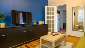 A modern living room with a flat-screen TV on a dark cabinet, a small table with books, a potted plant, and a door leading to another room. - Cozy Condesa (Mexico City)