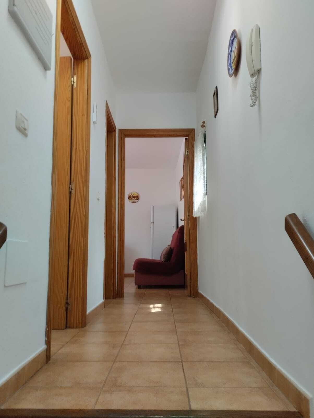 A hallway with a red sofa, a wooden door, and a white wall with a telephone and a picture frame.